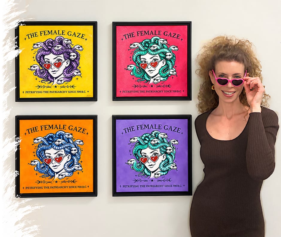 Lauren Farrow in heart-shaped pink sunglasses standing beside her four framed Female Gaze Medusa paintings in yellow, magenta, orange and purple